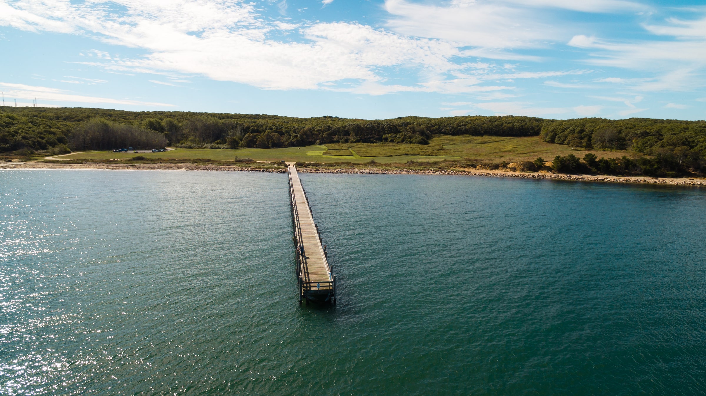 Aerial photograph of a long wooden pier extending from a wooded shoreline into blue water