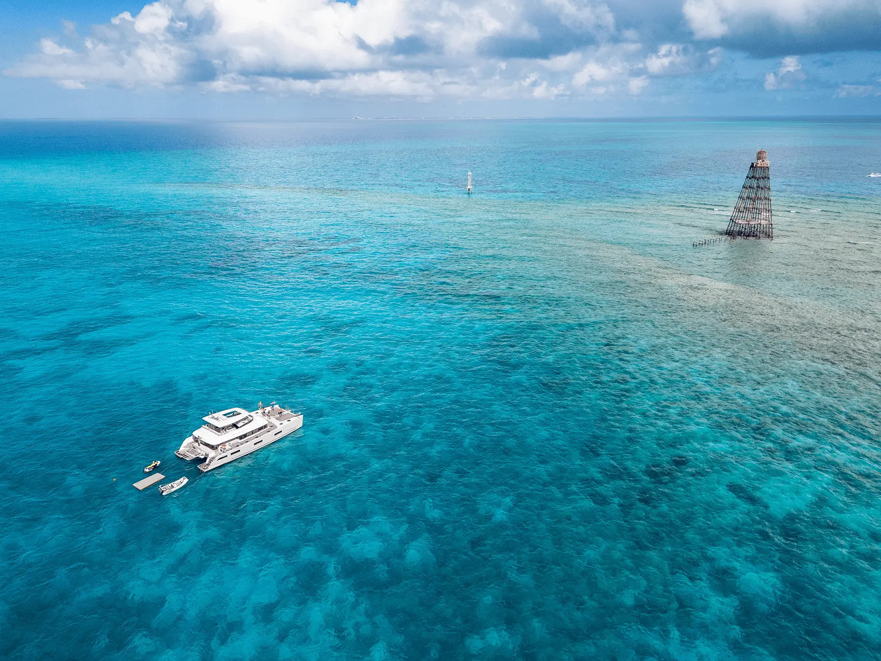 Atlantia anchored in turquoise water near a lighthouse, with a tender and water toys alongside
